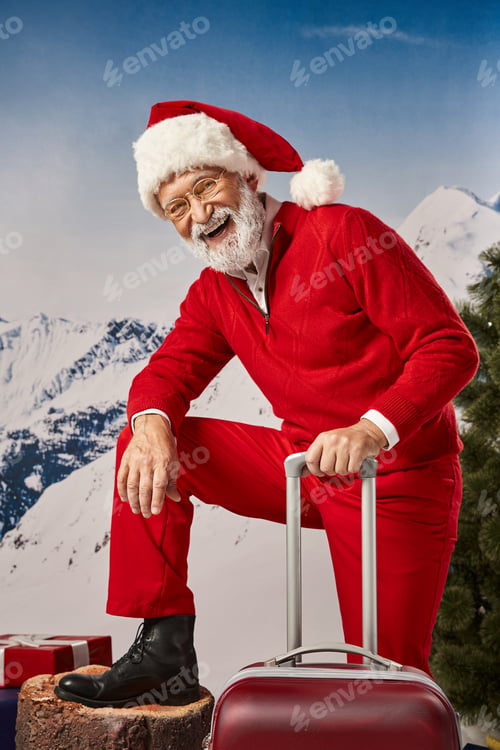 Preview: happy man in Santa costume with suitcase wearing glasses and smiling at camera, winter concept