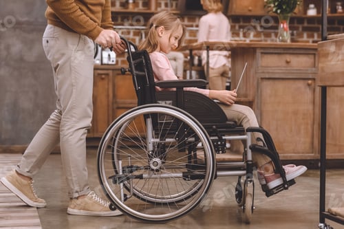Preview: cropped shot of father carrying wheelchair with cute little daughter using laptop at home