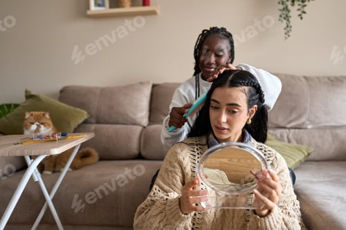 Preview: Young woman getting hair brushed by friend at home