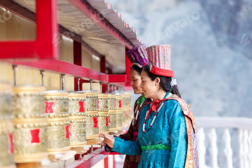 Preview: Two Indian women in traditional Leh attire spin golden prayer wheels at a monastery