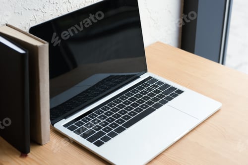 Preview: close-up view of laptop with blank screen and books on wooden table
