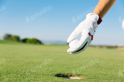 Preview: Woman´s hand putting a golf ball into hole.