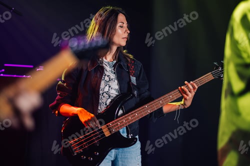 Preview: Female musician playing bass guitar on stage during concert