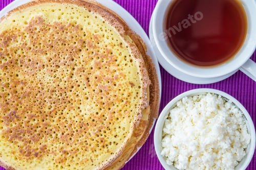 Preview: Pile of golden pancakes with cottage cheese and cup of tea. The top view.