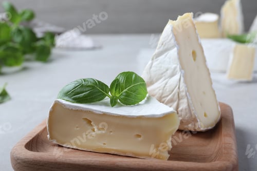 Preview: Delicious brie cheese with basil on light grey table, closeup