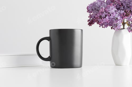Preview: Black mug mockup with a book and a bouquet of lilac in a vase on a white table.