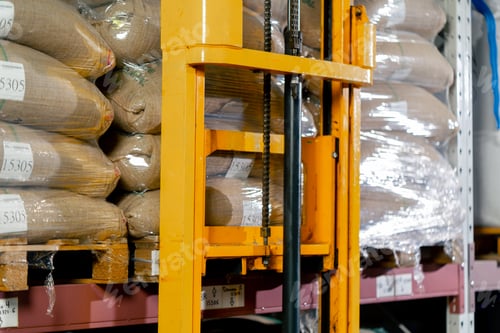 Preview: close up A worker at coffee factory uses a yellow lifting fork to lift and insert forks into pallets