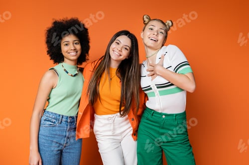 Preview: Smiling blonde teenager in casual outfit hugging interracial girlfriends with bold makeup and