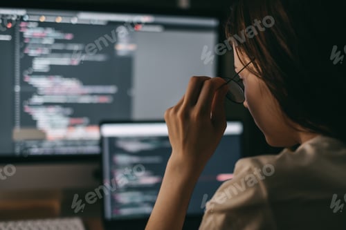 Preview: Young caucasian female programmer in glasses writes program code on a laptop computer. home office