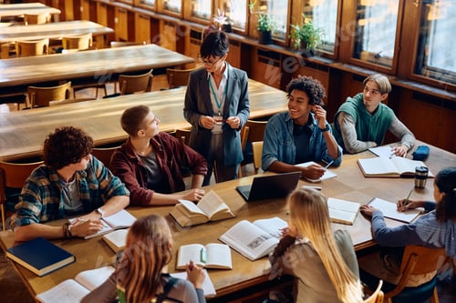 Preview: Happy high school teacher talking to group of students during a lecture in the classroom.