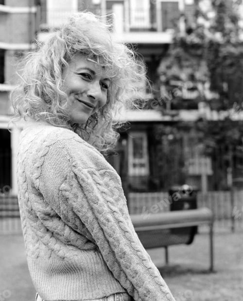 Preview: Smiling curly woman looking at camera in front of building.