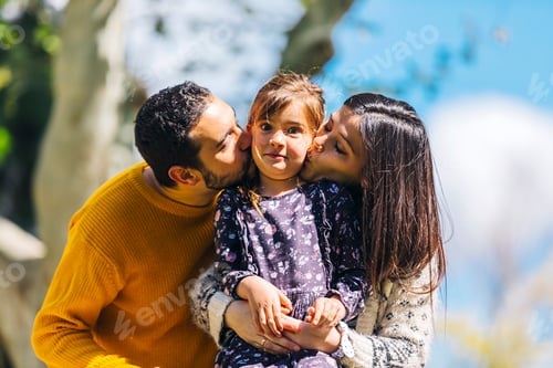 Visualização: Vista frontal de pais felizes beijando sua adorável filha ao ar livre no parque em um dia ensolarado
