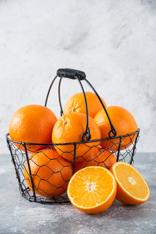 Preview: A metallic black basket full of juicy orange fruit on stone background
