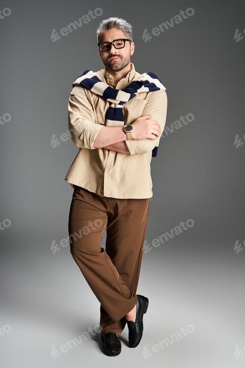 Preview: Stylish man in elegant outfit with glasses poses confidently in a modern studio setting