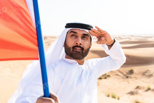 Preview: Middle-eastern emirati man wearing arab kandura holding emirati flag in the desert