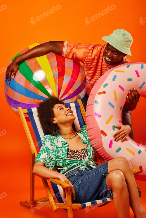 Preview: Positive young african american best friends in stylish summer outfit holding pool ball and ring