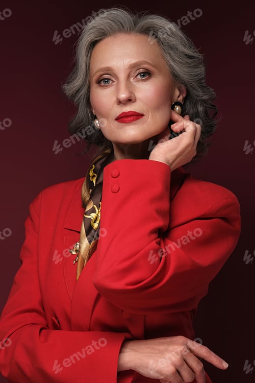 Preview: Portrait of a beautiful elderly womanin a red jacket with accessories, classic makeup and gray hair.