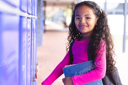 Preview: In school, young biracial female student holding books, standing by lockers outdoors