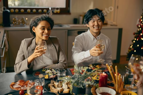 Preview: Smiling friends enjoying in conversation and drinking wine during Christmas party at home