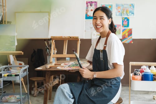 Preview: Young Asian female artist in art studio look at camera and smiling.