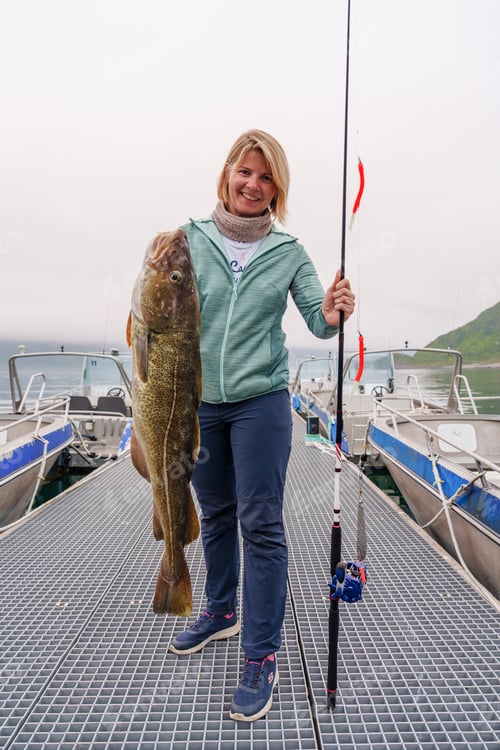 Preview: Happy Fisherwoman holding big arctic cod. Norway happy fishing. Woman with cod fish in hands