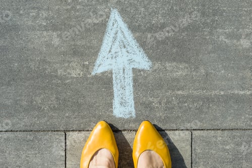 Preview: Female feet with arrow painted on the grey sidewalk