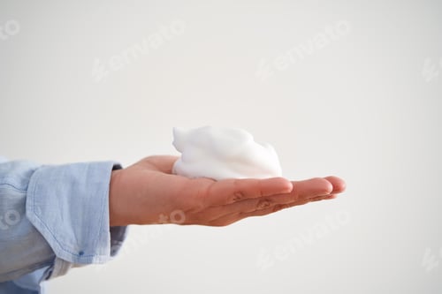 Preview: Hands in a blue shirt hold a savory facial foam demonstrating its texture.