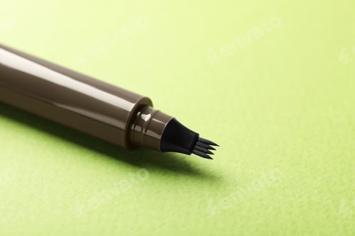 Preview: One liquid eyebrow pencil on green background, closeup. Space for text