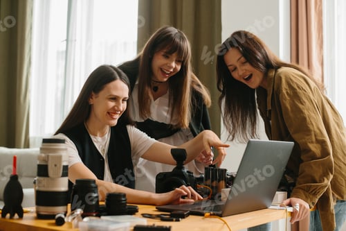 Preview: Young female photographer in photo studio shows photos on laptop to model and assistant.