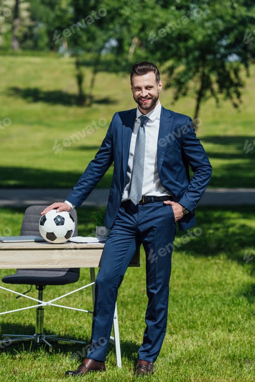 Preview: full length view of young businessman putting football on table while standing in park