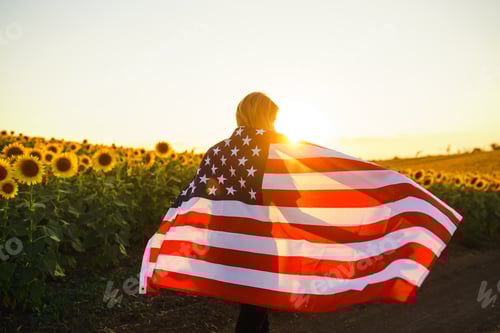 Preview: Beautiful girl with the American flag in a sunflower field. 4th of July. Fourth of July. Freedom.