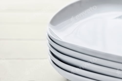 Preview: Stack pile of rectangular white ceramic dishes with rounded edges on wooden white background.