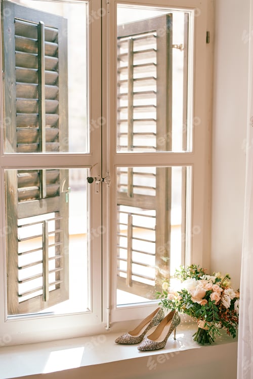 Preview: Bride shoes with a bouquet of flowers stand on the windowsill in the room