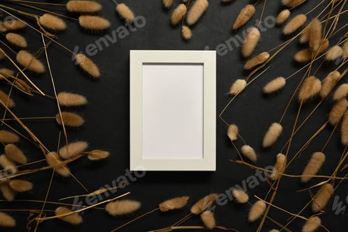 Preview: White picture frame surrounded by dried fluffy bunny tails grass on black background.