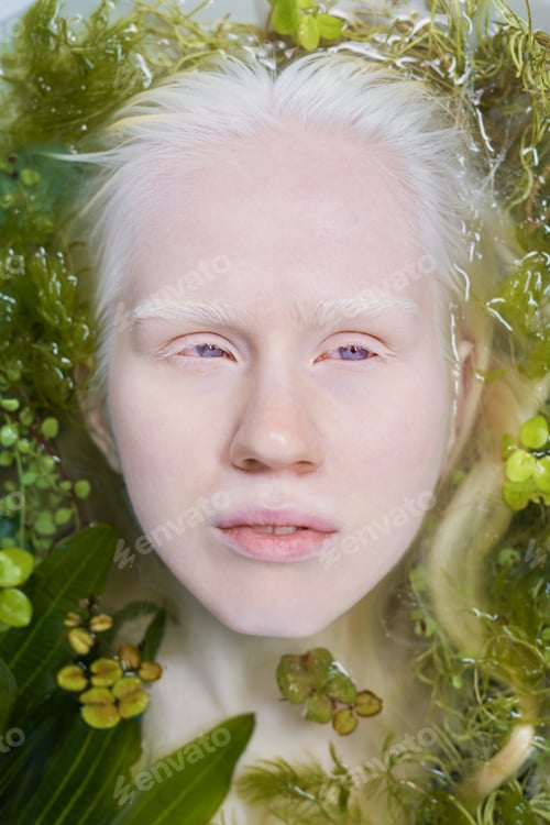 Preview: Above view of face of young albino woman lying in pure water with green plants