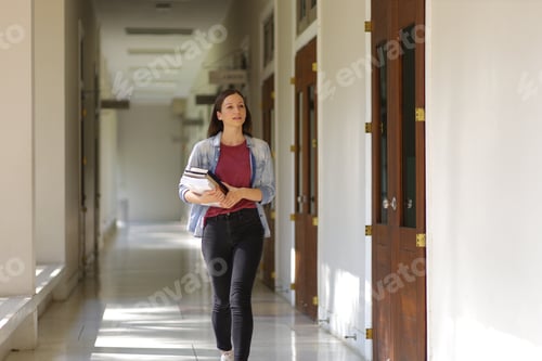 Preview: Female university student holding a textbook walking on the corridor of the school building.