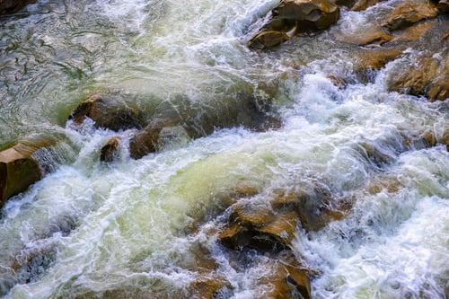 Preview: Aerial view of river waterfall with clear turquoise water falling down between wet boulders