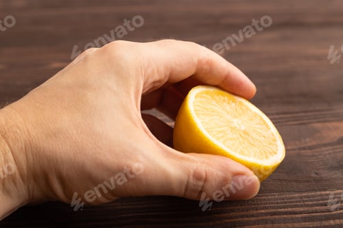 Preview: Yellow Lemon Cut in half with hand on brown wooden, Side view, close up