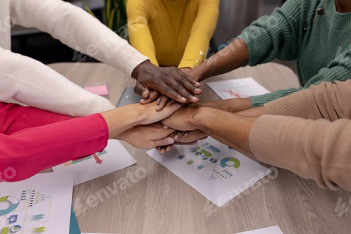 Preview: Cropped hands of multiracial male and female advisors stacking hands over conference table in office