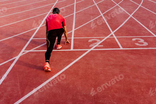 Preview: young muscular athlete is at the start of the race tracks line at the stadium. Sports concept