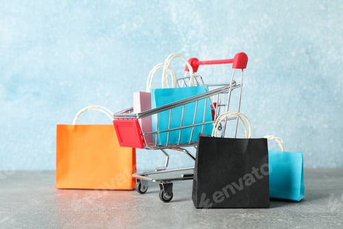 Preview: Small shopping cart and paper bags on grey background, copy space