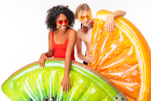 Preview: Young african female and caucasian blonde man stands in swimsuit with big rubber beach mattresses