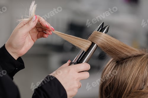 Preview: professional hairdresser curls hair with a curling iron in a beauty salon
