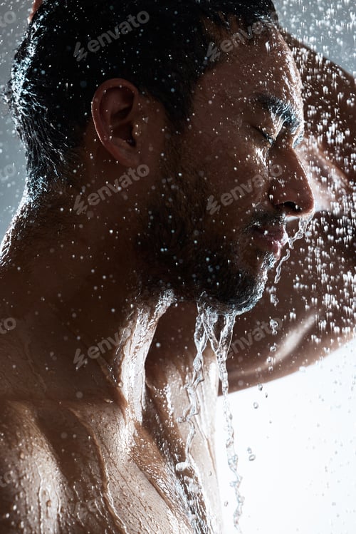 Preview: Studio shot of a young man washing his hair in a shower against a grey background