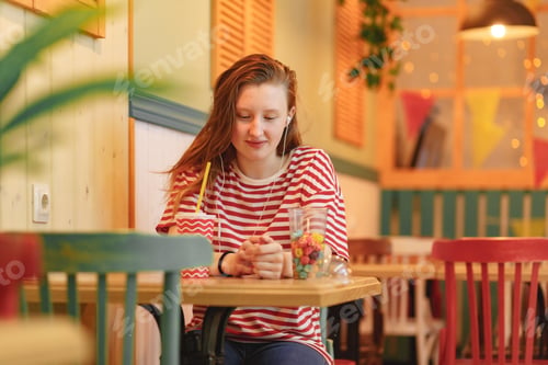 Preview: Young girl sitting in cafe, listening to music and drinking lemonade