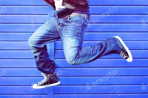 Preview: Man wearing denim and sneakers captured in a jump position, view of waist down only