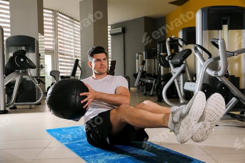 Preview: Muscular man exercising with medicine ball on mat in gym
