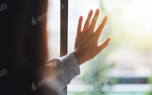 Preview: Rear view image of a sad woman touching on window while looking outside