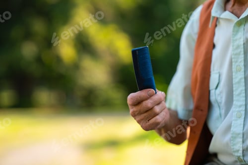 Preview: Senior man sitting on a bench in the park and holding comb. Elderly man grooming himself before