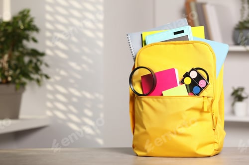 Preview: Yellow backpack with different school stationery on table indoors, space for text